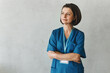 © shurkin_son - Tips and advice on health care from medical expert. Portrait of confident female doctor in blue uniform standing with folded arms isolated on gray background looking aside on copy space