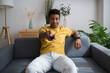 © Westend61 - Man sitting on sofa watching TV with remote in modern living room