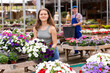 © JackF - Positive young female shopper in casual jeans and tank top selecting vibrant blooming Petunia atkinsiana plants in pots from array of colorful flowers at local garden center