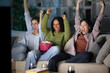 © Antonioguillem - Excited diverse friends watching sports on tv at home in the night
