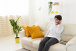 © satura_ - Woman talking on smartphone on white sofa in modern living room. Home communication, remote conversation, and digital lifestyle inside bright apartment interior.