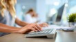 © Justlight - Focused view of a medical receptionist typing on a computer keyboard with blurred checkin forms and queuing screens in the background.