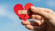 © Tatiana - Woman holding red broken heart shape with plaster on blue sky. Concept of healing emotional pain and mending relationship after breakup.