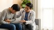© Artfinity - Professional doctor consulting a male patient in a clinic. Healthcare and stomach pain diagnosis. Asian physician comforting a young man holding his abdomen on a couch.