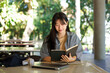 © Stella 16 - asian woman college student holding pen reading book over laptop at white table in building.