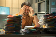 © Golf_MHNK - Hispanic accountant in crisis mode, battling worries about bankruptcy and financial issues while working overtime in a cluttered and stressful office environment.