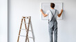 © Anastasiia Havelia - Faceless shot from behind: a person in overalls standing on a ladder, hanging a minimalist framed art piece on a white wall, decorating a new home, bright airy space, sharp focus o
