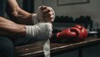 © thanawat - Close-up of a fighter wrapping hands, with boxing gloves nearby, set in a training environment emphasizing preparation and focus.