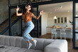 © Prostock-studio - Happy young Caucasian woman in wireless headphones enjoying music, dancing and jumping on sofa at home, free space. Portrait of joyful millennial lady listening to song, flying in air indoors