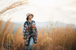 © chokniti - Woman traveler wearing colorful patterned sweater and hat standing in golden grass field under warm sunlight enjoying nature, outdoor adventure, and peaceful autumn atmosphere at countryside