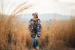© chokniti - Woman traveler wearing colorful patterned sweater and hat standing in golden grass field under warm sunlight enjoying nature, outdoor adventure, and peaceful autumn atmosphere at countryside