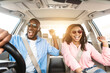 © Prostock-studio - Summer Holidays And Roadtrip Concept. Front view portrait of excited black couple in sunglasses driving car, dancing to music and singing favorite song, going on vacation for rest and relax, sun flare