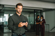© Stock 4 You - Man trader using digital technology cellphone phone mobile for business trade work. Focused young Latin businessman holding smartphone telephone device standing in office with people on background