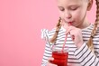 © New Africa - Little girl drinking fresh pomegranate juice on pink background, closeup. Space for text