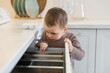 © New Africa - Child safety at home. Little boy opening drawer with utensils in kitchen