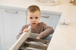 © New Africa - Child safety at home. Little boy opening drawer with utensils in kitchen