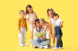 © Pixel-Shot - Group of little children with nursery teacher reading story on yellow background