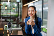 © amnaj - Asian businesswoman smiling, holding a cup of coffee. She is relaxing during a business break in a modern office or cafe