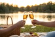 © Marina Shvedak - A man and woman toast with champagne flutes during a romantic picnic by a lake at sunset. Romantic date concept for anniversary.