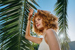 © SHOTPRIME STUDIO - curly woman with natural hair enjoys sunny day outdoors under tropical palm leaves in white sleeveless top, fresh, bright mood, summer vibes