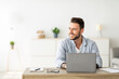 © Prostock-studio - Happy freelance man working on laptop in home office, sitting on workplace and looking aside at free space. Smiling guy thinking about successful business strategy or dreaming about holiday