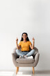 © Prostock-studio - Look At This. Happy Brunette Lady Sitting In Armchair And Pointing Up With Two Hands, Cheerful Millennial Woman Demonstrating Copy Space Above Her Head And Smiling At Camera, Vertical Shot