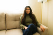 © AntonioDiaz - Latin woman relaxing on a sofa at home, smiling with long dark hair, enjoying comfortable domestic living