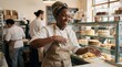 © ArtMajestic - Black woman baker laughing while dusting flour off hands in busy bakery kitchen. Small business success and happy employee lifestyle