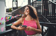 © BullRun - Young smiling woman holding smartphone, enjoying sunny day outdoors. Candid moment of digital connection, joyful mood, casual lifestyle, summer vibe, mobile-first generation.