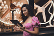 © BullRun - Smiling Hispanic woman in pink floral dress using tablet with stylus outdoors, representing digital creativity, freelance work, and independence in connected modern lifestyle.