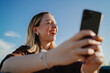© BullRun - Happy young woman laughing while taking selfie with smartphone outdoors, enjoying digital communication, mobile connection and modern lifestyle in urban environment.