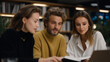 © forenna - Warm lamp light spills over a bookshelf as senior mentors offer feedback and the team asks questions, agendas updated and mentorship noted during a home office meeting about career growth.