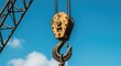 © rahayu - A close-up of a yellow and black hook on a construction crane against a blue sky with a few small clouds