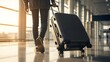 © Artfinity - Traveler pulling a black suitcase in airport terminal. Vacation trip and international flight. Person walking toward boarding gate with rolling luggage during golden hour sunset