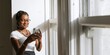 © Rawpixel.com - A young African American woman smiling and using a smartphone. The woman is standing by a window, enjoying her smartphone. She is wearing glasses. African American influencer woman on social media.