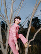 © SHOTPRIME STUDIO - Pink fashion portrait among leafless branches, creative silhouette and whimsical vibe, a model in soft pink suit climbing a tree with floral glasses under clear sky