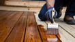 © olgakris - Wood deck staining process with a brush, home improvement, protective coating, wooden surface maintenance, outdoor decking renovation, applying varnish, house exterior carpentry work