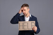 © New Africa - Unhappy businessman holding cardboard sign with word Help on grey background