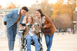 © Pixel-Shot - Young woman in wheelchair and her friends with coffee taking selfie on city square