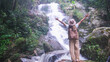 © Farknot Architect - Rear view image of a woman with opened hands standing in front of the waterfall in the forest