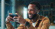 © peopleimages.com - Gaming, smartphone and man with earphones, home and listening to audio on break, laughing and online. Happy, gamer and black person with mobile for entertainment, esports and tech for sound in house