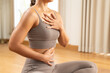 © Leny Studio - Woman practicing mindful breathing in neutral activewear with hand on chest and abdomen in bright living room