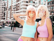 © halayalex - Two young beautiful smiling hipster female in trendy summer clothes. Sexy carefree women posing in the street in wigs. Positive funny models having fun at sunset. Blowing bubble with chewing gum
