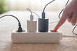 © Nanci - Human hand is switching off a white power strip, with multiple plugs and chargers connected, illustrating the concept of saving energy and reducing electricity consumption