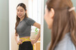 © Pormezz - Weight lose, loss concept. Slim body asian young woman hand use tape measuring around waistline in fit sports. Girl looking reflect in mirror at home. Healthy nutrition, fitness for wellbeing beauty.