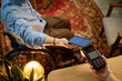 © Seventyfour - Middle aged Caucasian man with disability sitting in wheelchair holding smartphone making contactless payment at point of sale terminal, female hand holding card reader in foreground