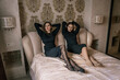 © svetograph - Women Dresses Bedroom Posing: Twin Models in Black Dresses Relaxing on Bed, Indoors, Present Day, Fashion Photography.