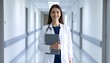 © StocksJust4You - Confident young female doctor standing at hospital corridor, holding medical records, professional attire
