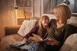 © Stockphotodirectors - A woman reads a book to a smiling girl while they sit together on a sofa. The warm atmosphere is enhanced by soft lighting and cozy decor. They share a joyful connection.