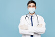 © ViDi Studio - Young male doctor man wear white medical gown suit sterile mask work in hospital clinic office hold hands crossed folded isolated on plain blue background studio portrait. Healthcare medicine concept.